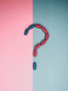 Creative arrangement of red and blue pills forming a question mark on split pink and blue background.